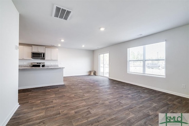 unfurnished living room featuring plenty of natural light and dark hardwood / wood-style flooring