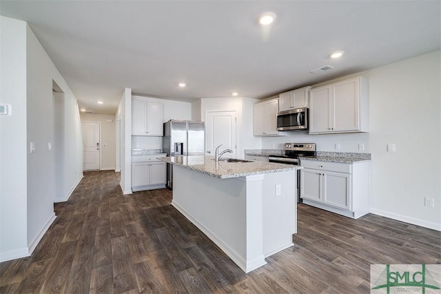 kitchen with appliances with stainless steel finishes, dark hardwood / wood-style floors, white cabinetry, and a kitchen island with sink