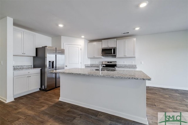 kitchen with light stone countertops, stainless steel appliances, dark wood-type flooring, a center island with sink, and white cabinetry