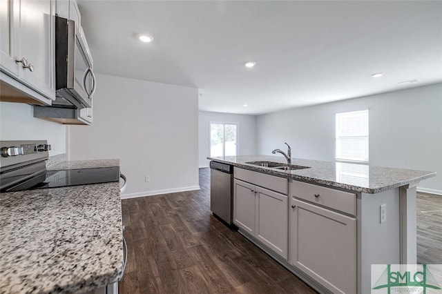 kitchen featuring dark hardwood / wood-style flooring, light stone countertops, a center island with sink, and appliances with stainless steel finishes