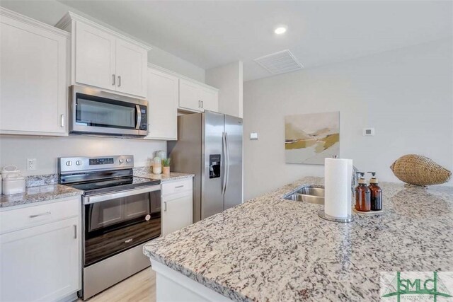 kitchen featuring white cabinetry, light wood-type flooring, light stone counters, and appliances with stainless steel finishes