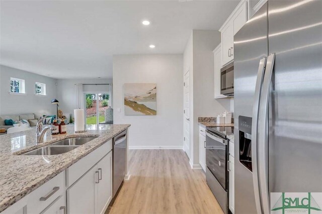 kitchen featuring sink, light stone countertops, appliances with stainless steel finishes, light hardwood / wood-style floors, and white cabinetry