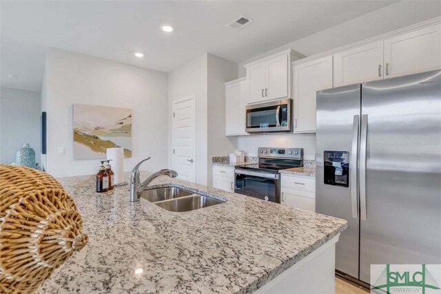 kitchen with kitchen peninsula, appliances with stainless steel finishes, light stone counters, sink, and white cabinetry