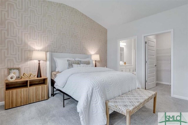 bedroom featuring carpet, vaulted ceiling, ensuite bath, and a spacious closet