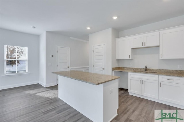 kitchen with white cabinets, sink, light stone countertops, light hardwood / wood-style floors, and a kitchen island