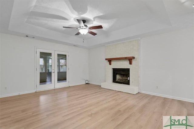 unfurnished living room with french doors, ceiling fan, a raised ceiling, and light hardwood / wood-style flooring