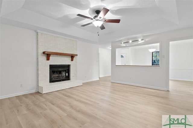 unfurnished living room featuring a tray ceiling, a fireplace, light hardwood / wood-style floors, and ceiling fan