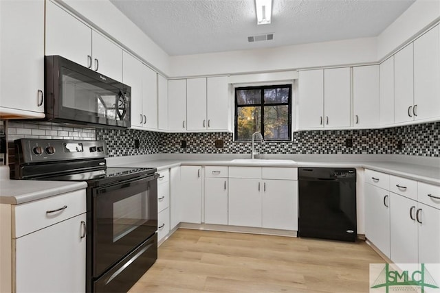 kitchen with sink, black appliances, white cabinets, decorative backsplash, and light wood-type flooring