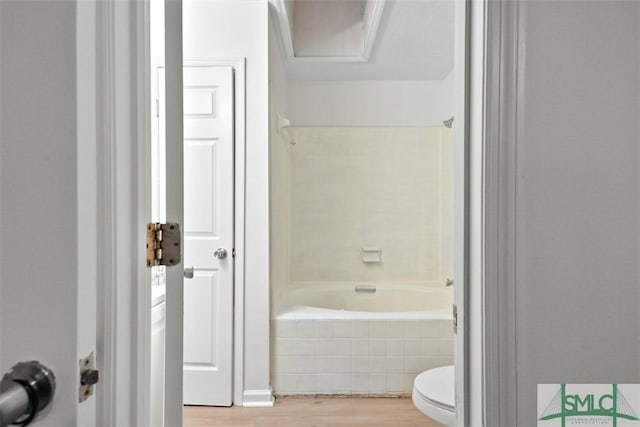 bathroom with hardwood / wood-style flooring, tiled shower / bath, and toilet