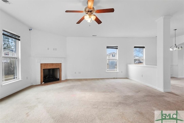 unfurnished living room featuring a tile fireplace, light carpet, and ceiling fan with notable chandelier