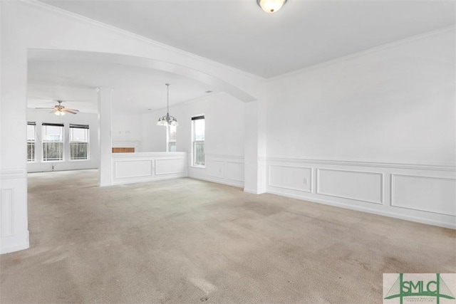 carpeted empty room featuring ceiling fan with notable chandelier and crown molding