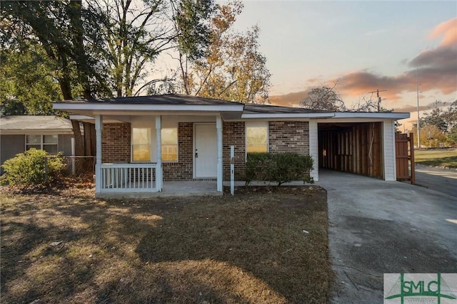 ranch-style home featuring a carport, covered porch, and a lawn