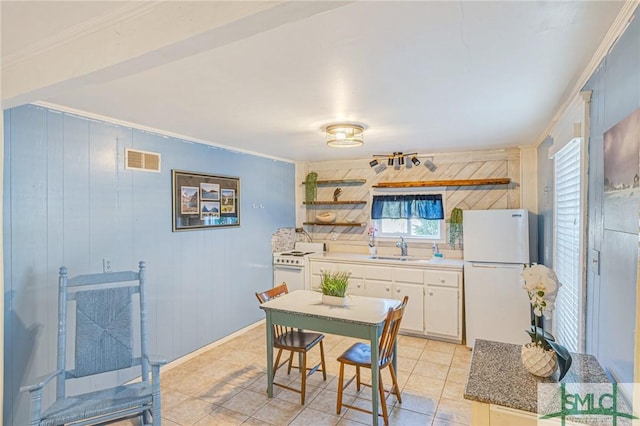 kitchen featuring wooden walls, sink, light tile patterned flooring, and white appliances