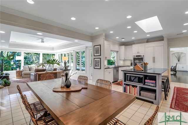 dining space with light tile patterned floors, a skylight, ceiling fan, and crown molding