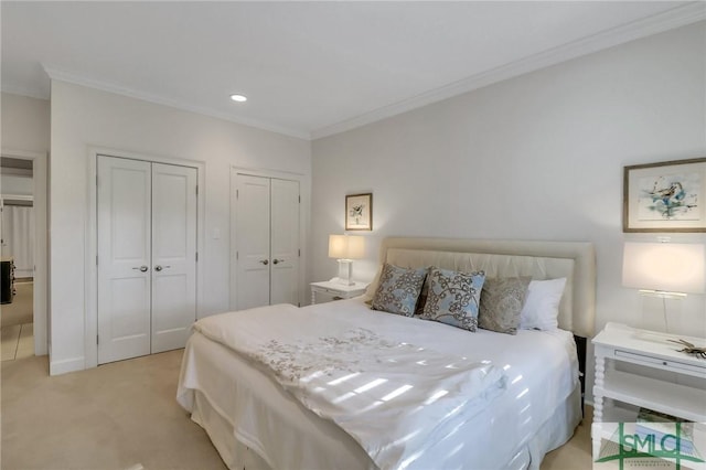 bedroom featuring ornamental molding, light carpet, and two closets