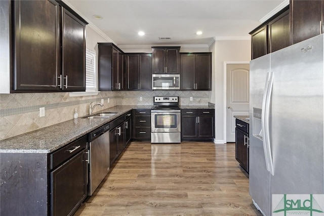 kitchen featuring sink, tasteful backsplash, dark stone countertops, light hardwood / wood-style floors, and appliances with stainless steel finishes