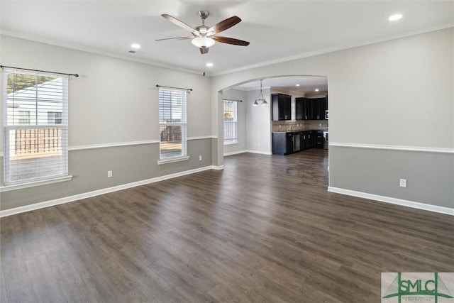 unfurnished living room with dark wood-type flooring, ceiling fan with notable chandelier, and ornamental molding