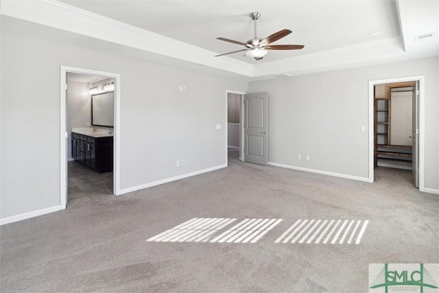 unfurnished bedroom featuring a raised ceiling, ensuite bathroom, ceiling fan, and light colored carpet