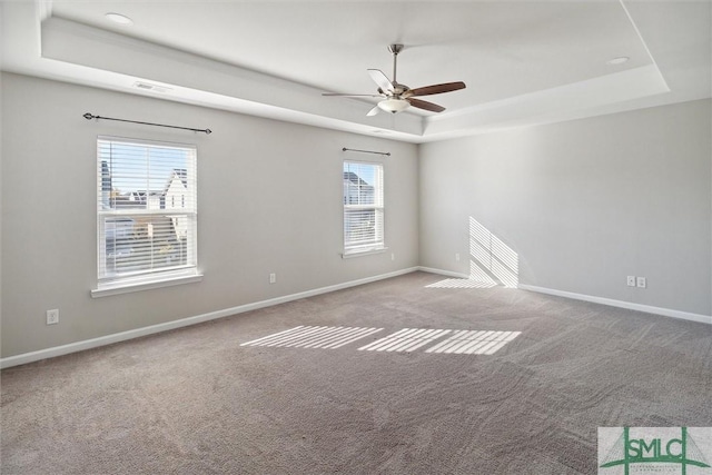 empty room with light colored carpet, a raised ceiling, plenty of natural light, and ceiling fan