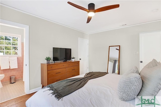 bedroom featuring connected bathroom, light hardwood / wood-style flooring, ceiling fan, and crown molding