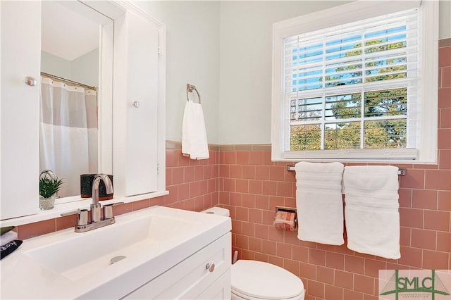 bathroom featuring vanity, a healthy amount of sunlight, toilet, and tile walls