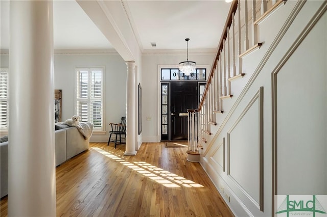 foyer featuring a chandelier, light hardwood / wood-style flooring, ornamental molding, and ornate columns