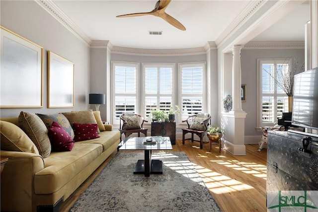 living room with decorative columns, ceiling fan, crown molding, and light wood-type flooring