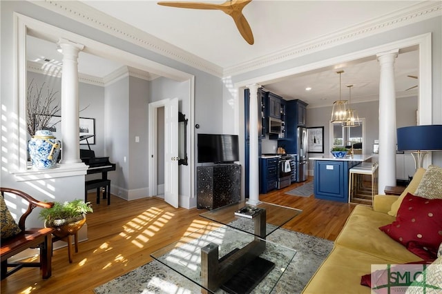 living room featuring ceiling fan with notable chandelier, light wood-type flooring, crown molding, and ornate columns