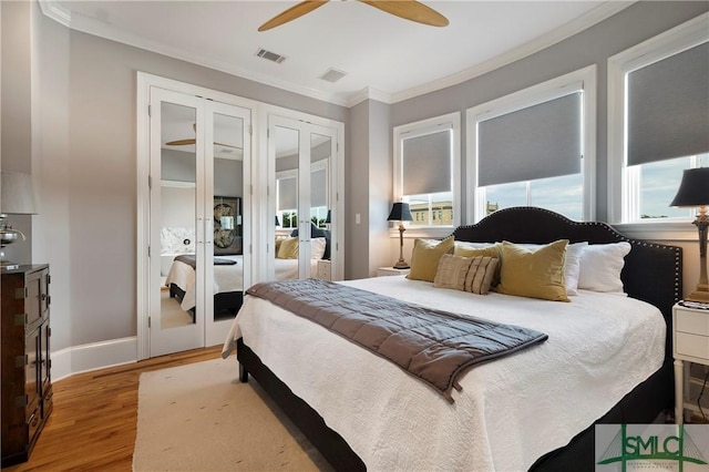 bedroom featuring multiple closets, light wood-type flooring, ceiling fan, and ornamental molding