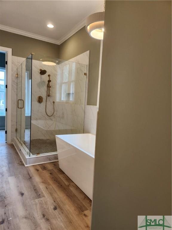 bathroom with a stall shower, a soaking tub, crown molding, and wood finished floors