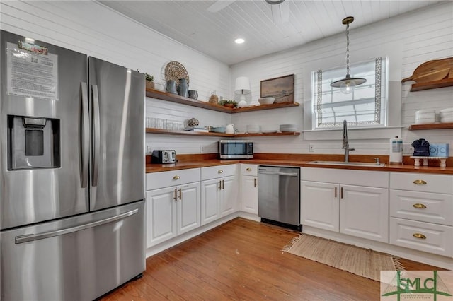 kitchen featuring sink, butcher block countertops, decorative light fixtures, white cabinets, and appliances with stainless steel finishes