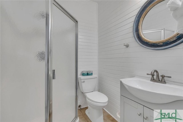 bathroom featuring vanity, a shower with door, wooden walls, tile patterned flooring, and toilet