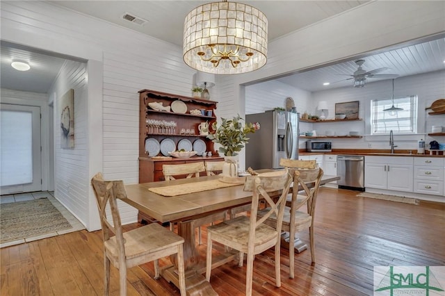 dining space featuring ceiling fan with notable chandelier, wood walls, wood-type flooring, and sink