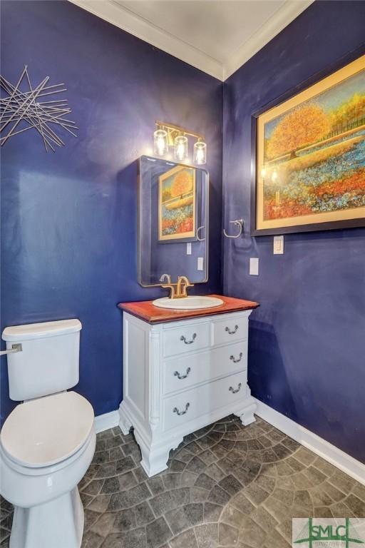 half bath featuring stone finish flooring, baseboards, toilet, and vanity