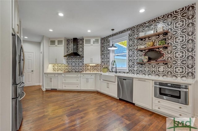 kitchen with a sink, stainless steel appliances, dark wood-type flooring, light countertops, and wall chimney range hood