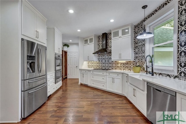 kitchen featuring a sink, dark wood-style floors, stainless steel appliances, wall chimney range hood, and glass insert cabinets