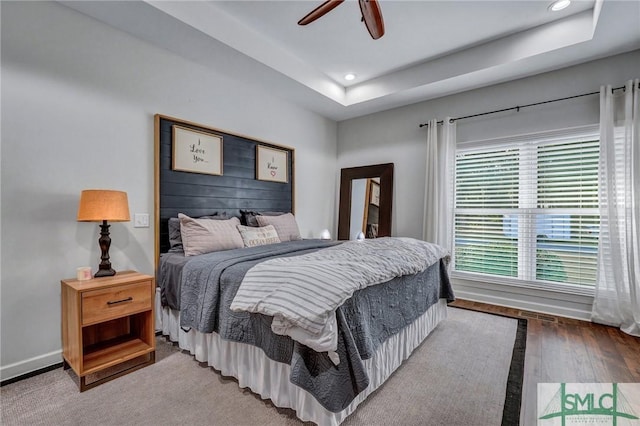 bedroom with a raised ceiling, wood finished floors, recessed lighting, and baseboards