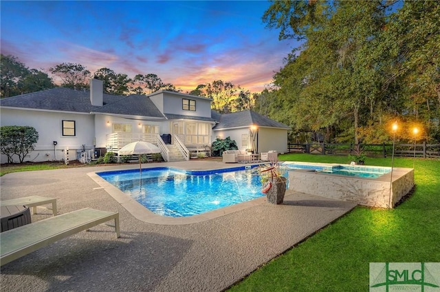 pool at dusk with an in ground hot tub, a lawn, and a patio area