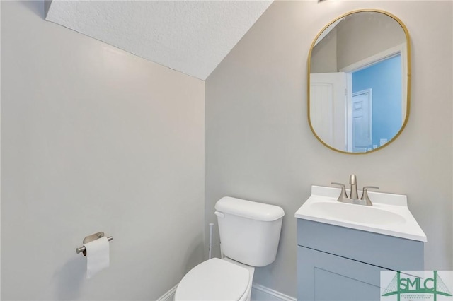 bathroom with vaulted ceiling, vanity, a textured ceiling, and toilet