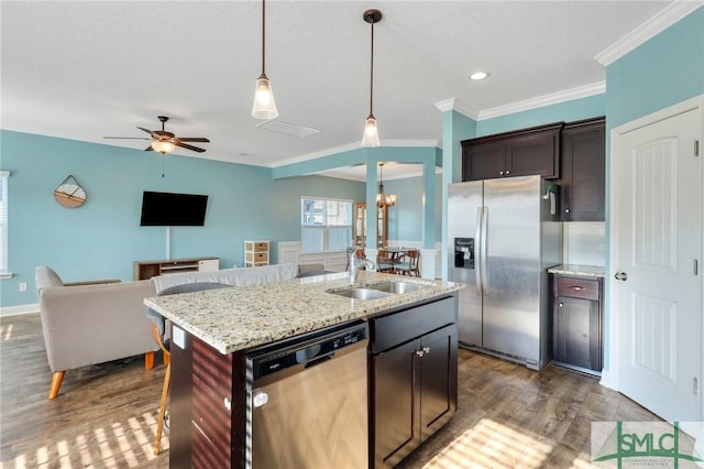 kitchen with sink, hanging light fixtures, stainless steel appliances, light stone counters, and a kitchen island with sink