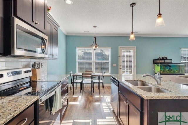 kitchen featuring decorative light fixtures, sink, stainless steel appliances, and a kitchen island with sink