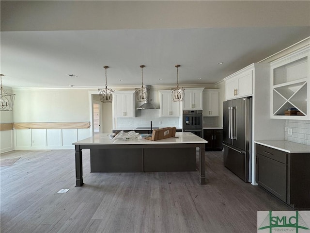 kitchen with a breakfast bar, high end fridge, hanging light fixtures, a kitchen island with sink, and white cabinets