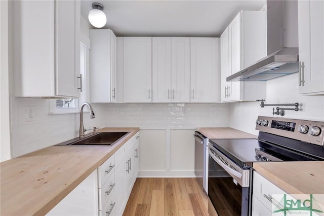 kitchen with white cabinets, sink, wall chimney exhaust hood, appliances with stainless steel finishes, and butcher block counters