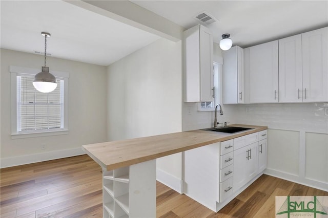 kitchen with wood counters, white cabinets, sink, light hardwood / wood-style flooring, and decorative light fixtures