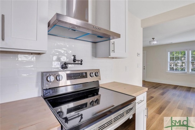 kitchen featuring white cabinets, electric stove, wall chimney range hood, light hardwood / wood-style flooring, and tasteful backsplash