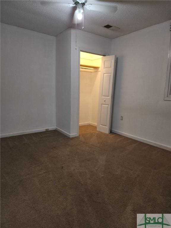 unfurnished bedroom featuring a textured ceiling, a closet, dark carpet, and ceiling fan