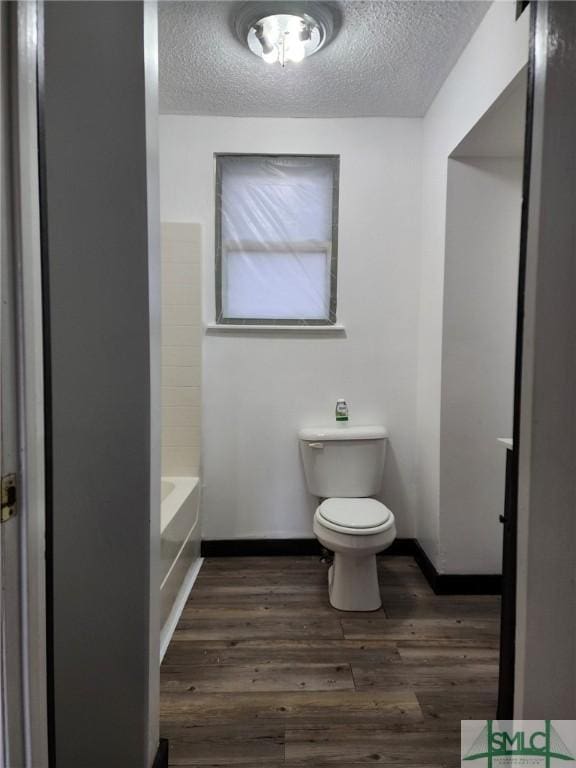 bathroom with hardwood / wood-style floors, toilet, a textured ceiling, and a tub