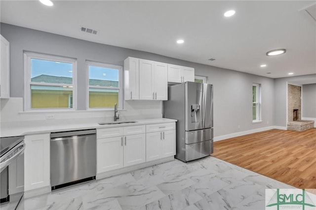 kitchen featuring white cabinetry, sink, stainless steel appliances, a brick fireplace, and light hardwood / wood-style floors