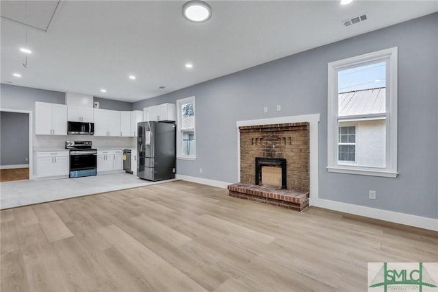 kitchen featuring light wood-type flooring, white cabinetry, stainless steel appliances, and a brick fireplace