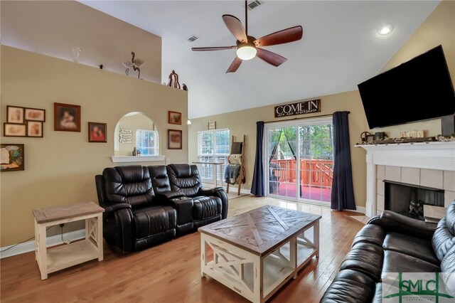 living room with ceiling fan, a fireplace, vaulted ceiling, and light wood-type flooring